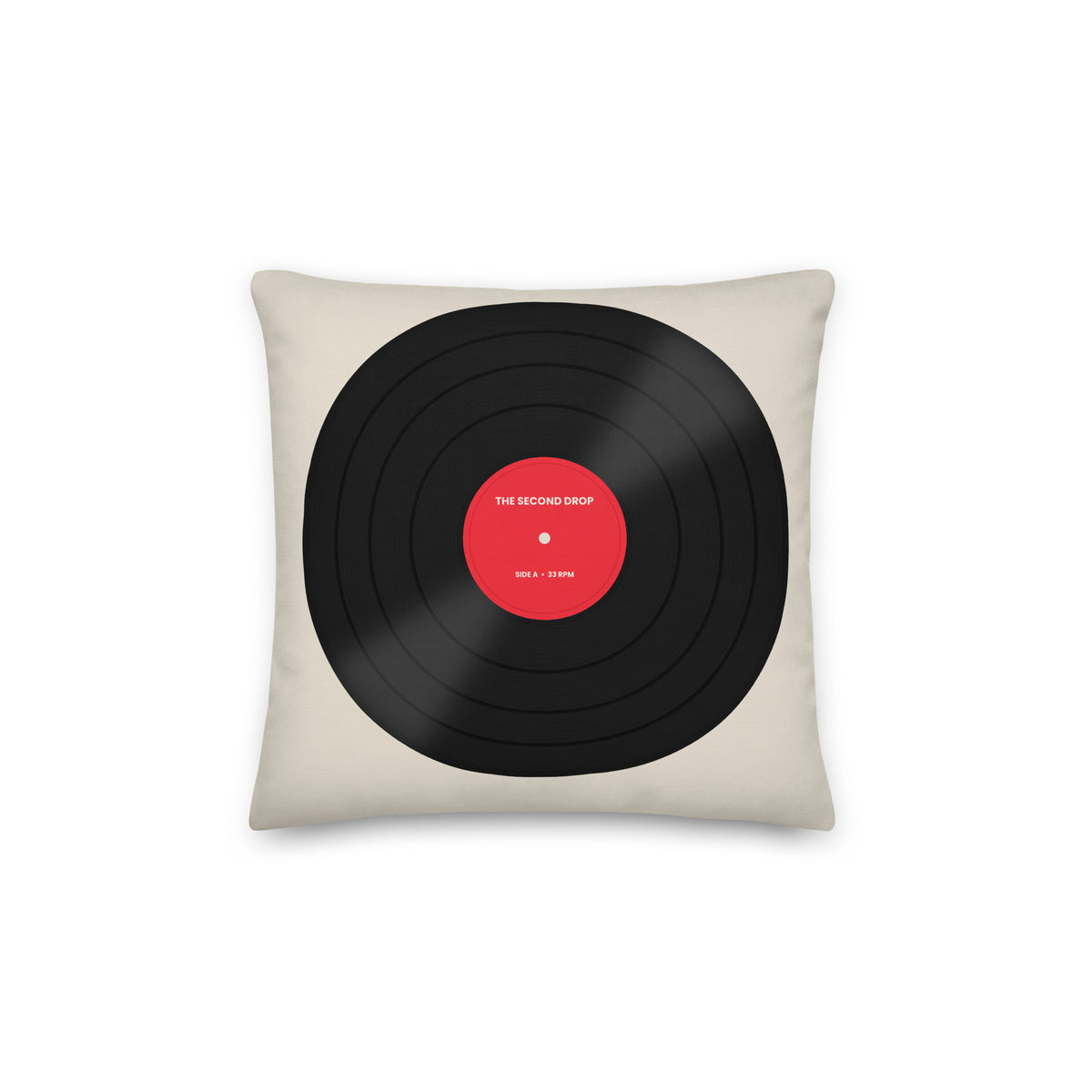 A square throw pillow in a light beige fabric, featuring a graphic print of a black vinyl record with a red center label that reads 'THE SECOND DROP