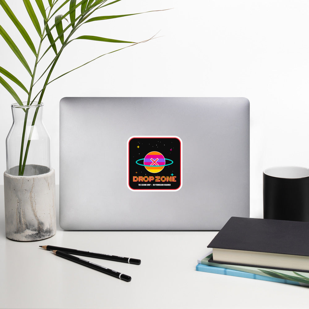 The Drop Zone - No Permission Required-The Second Drop-Laptop with a sticker on a desk with a plant, pencils, and books.