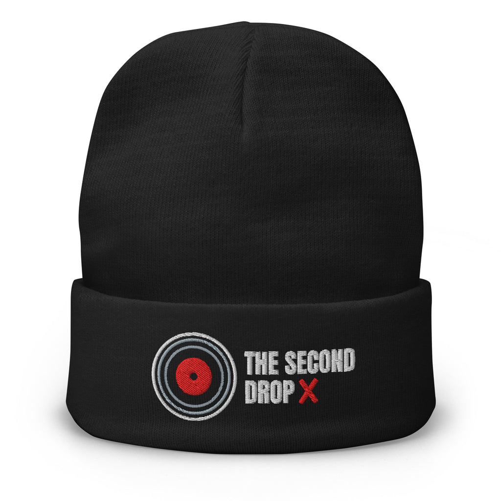 A black knit beanie with a folded cuff featuring an embroidered logo and text. The logo shows a red center with white and gray concentric rings, next to the text 'THE SECOND DROP X' in white and red.