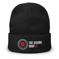 A black knit beanie with a folded cuff featuring an embroidered logo and text. The logo shows a red center with white and gray concentric rings, next to the text 'THE SECOND DROP X' in white and red.