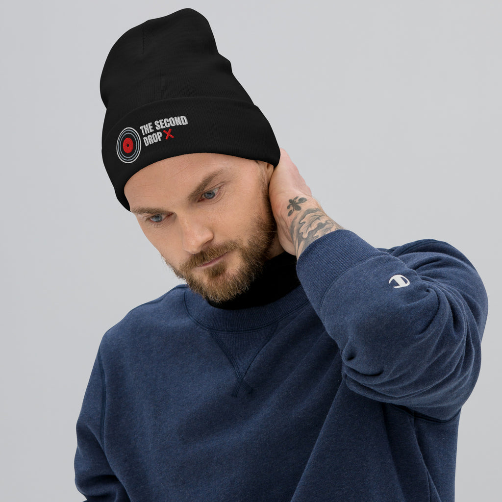 Man wearing a black beanie with 'THE SECOND DROP  text and a blue sweatshirt on a gray background