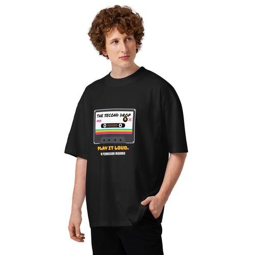 A person modeling an oversized black t-shirt with a retro cassette tape graphic that reads 'THE SECOND DROP. PLAY IT LOUD"