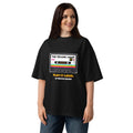 A woman modeling an oversized black t-shirt with a retro cassette tape graphic that reads 'THE SECOND DROP. PLAY IT LOUD"